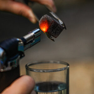 A Blow Torch Burning Coconut Charcoal Above A Glass of Water